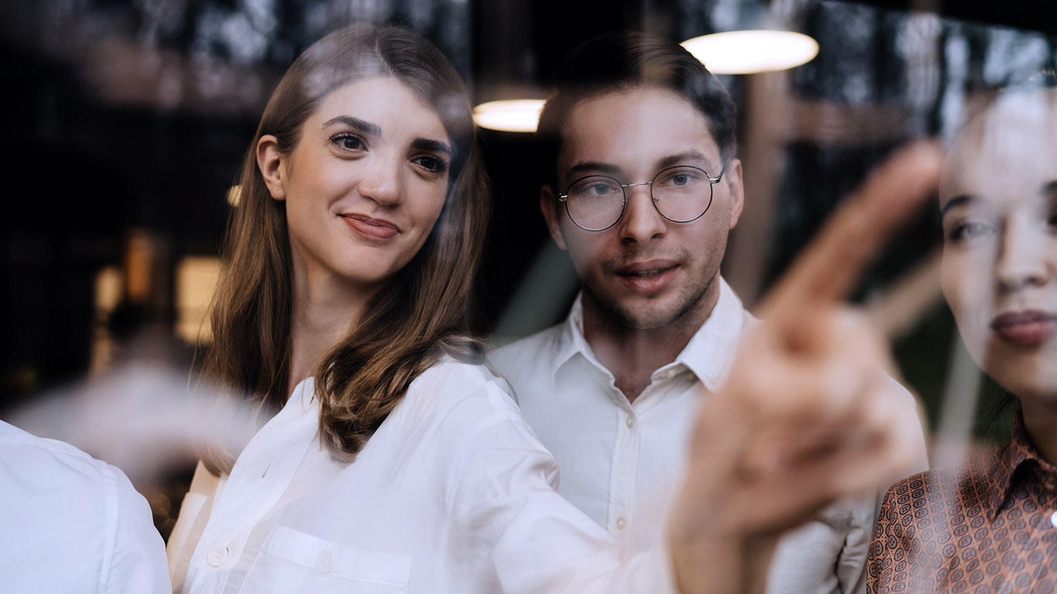 Smiling woman pointing at glass wall with co-workers