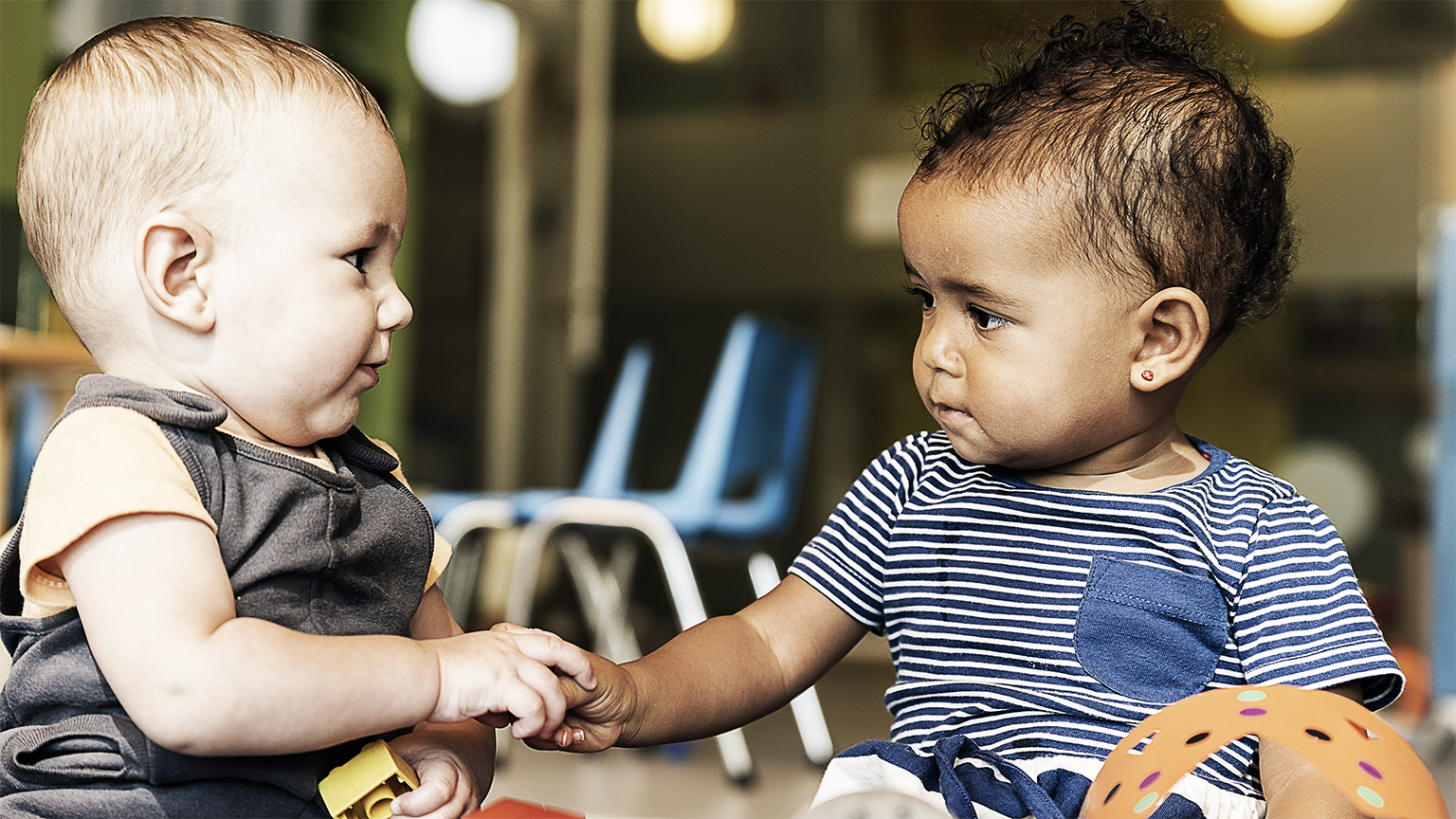 A pair of young children playing together, touching hands across the table