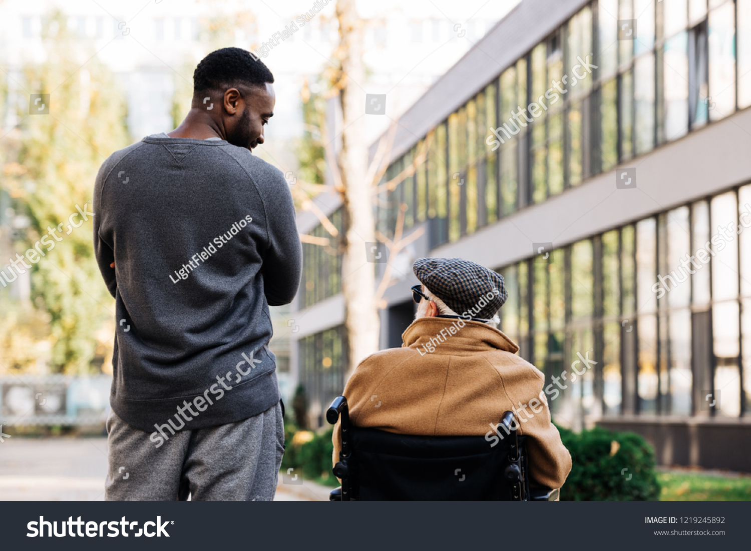 rear view of senior disabled man in wheelchair and african american man spending time together on street and looking at each othe