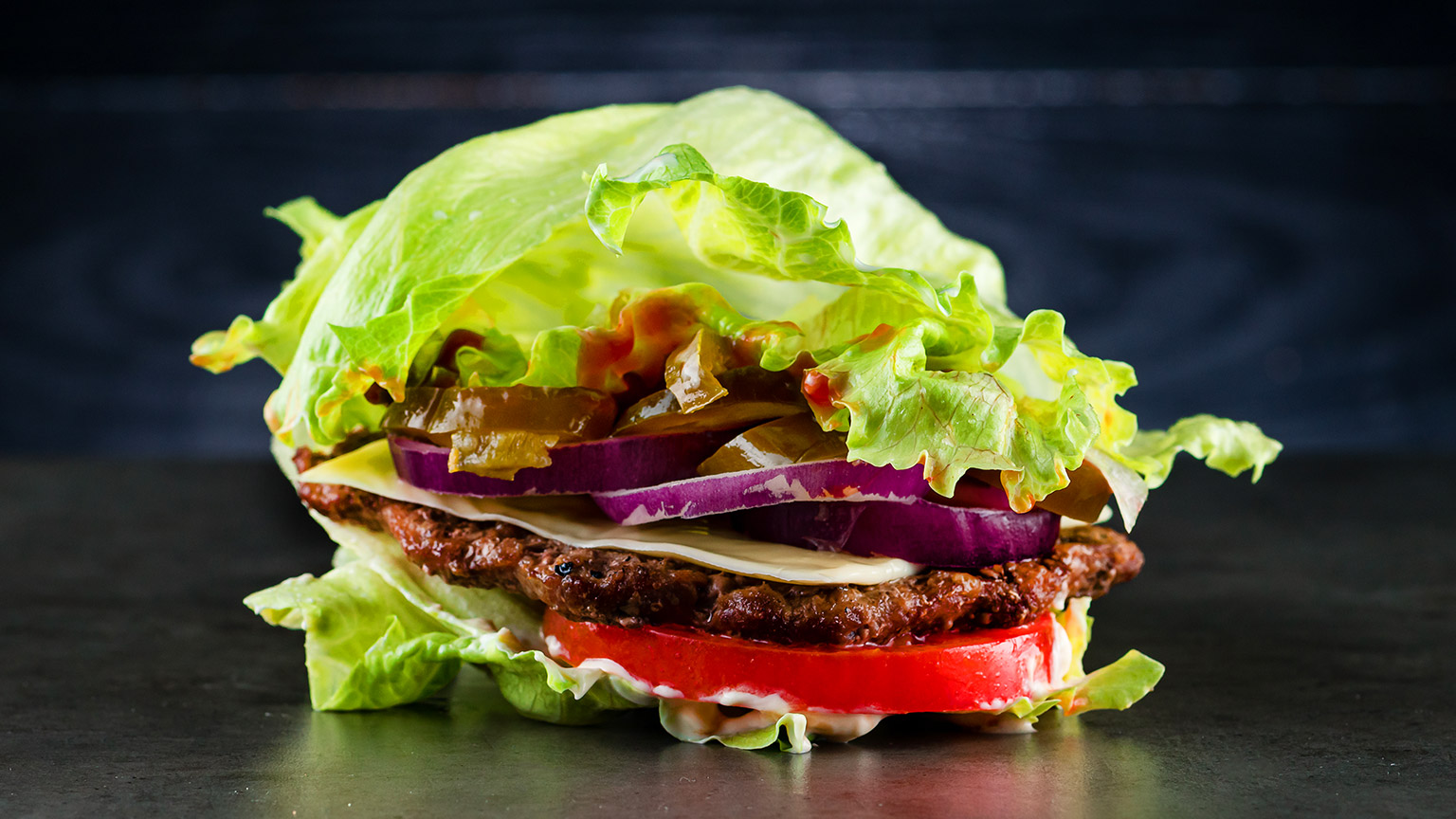 A burger wrapped in a lettuce leaf with various other toppings