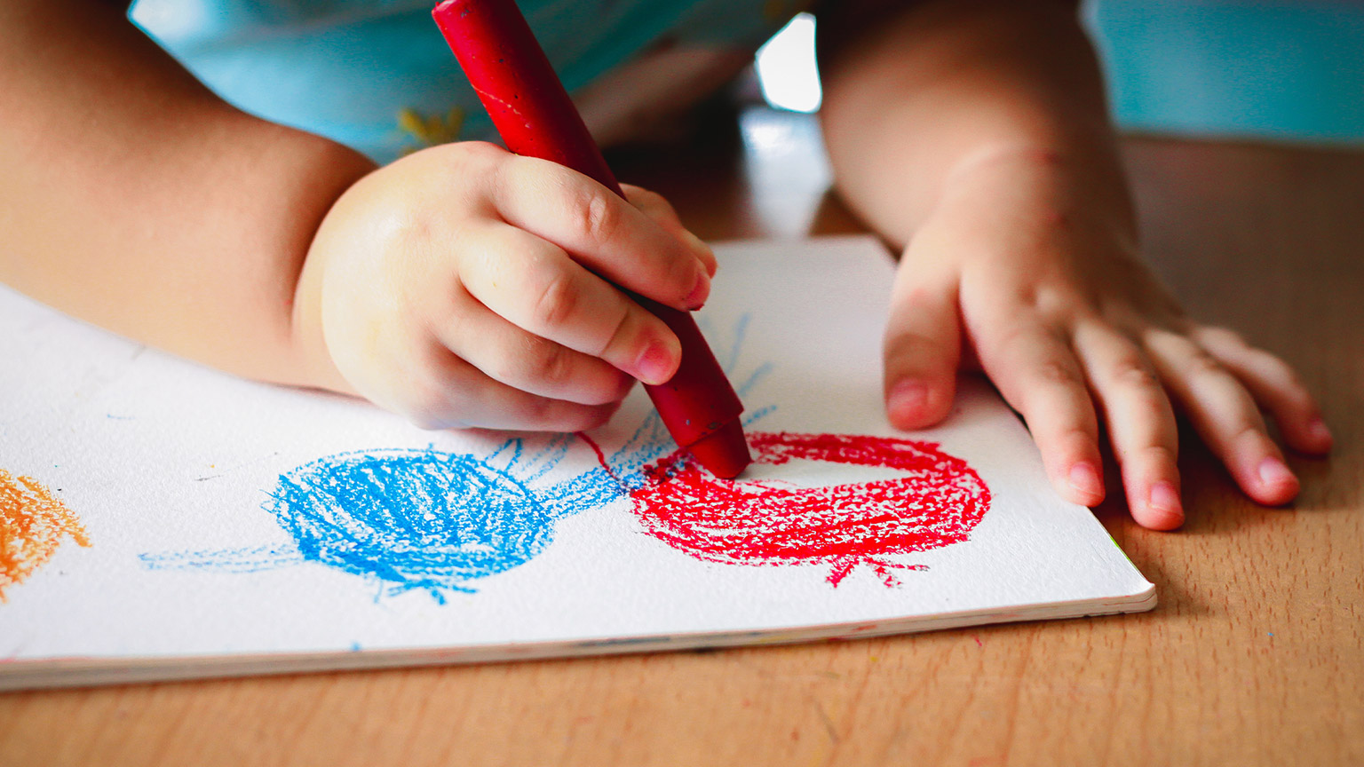 A close view of a child drawing with crayons