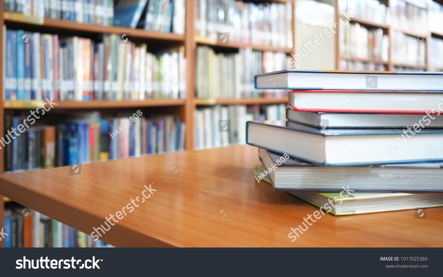 Book stack on wood desk and blurred bookshelf in the library room, education background, back to school concept