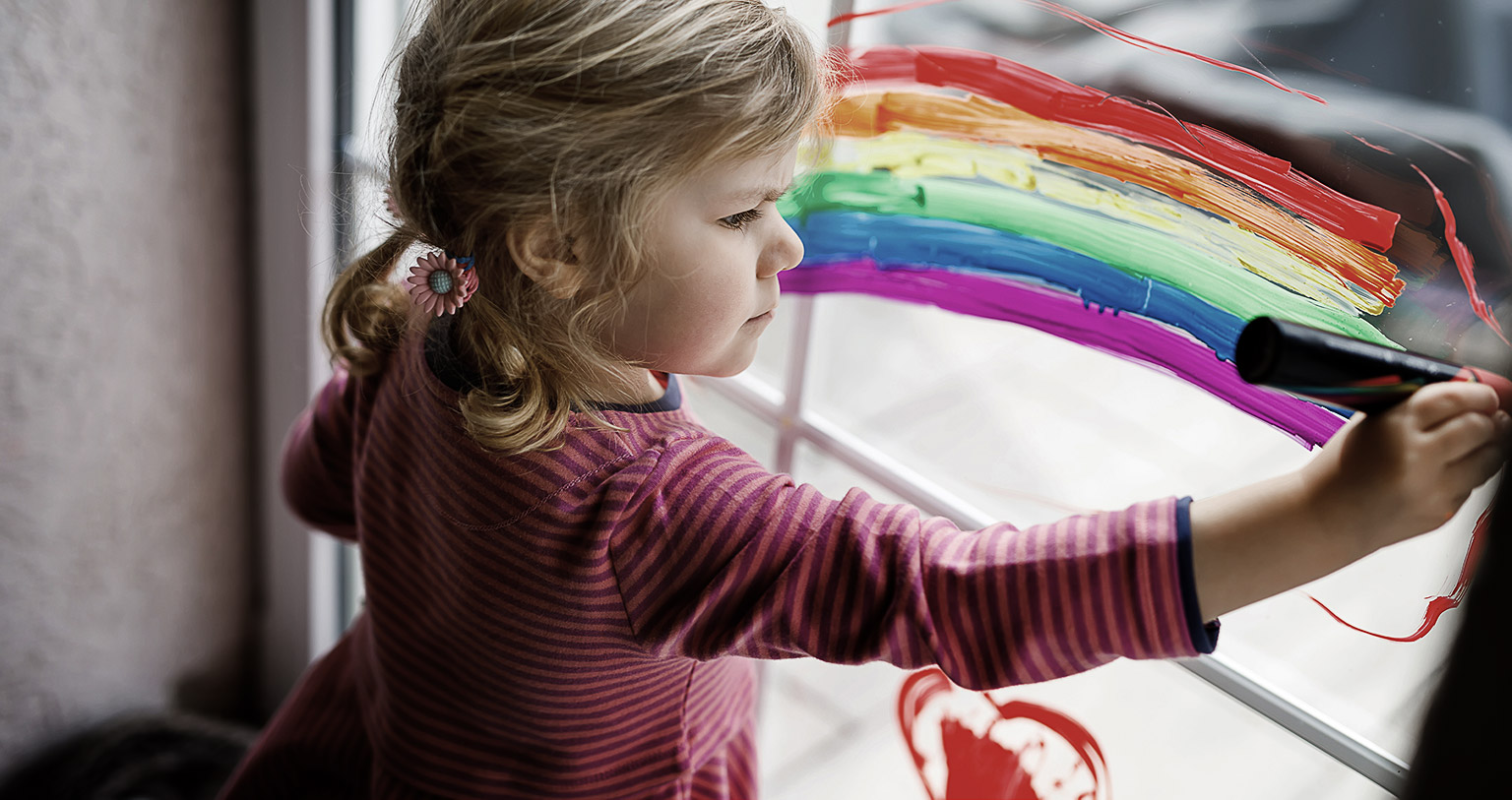 A girl painting a rainbow on a glass window