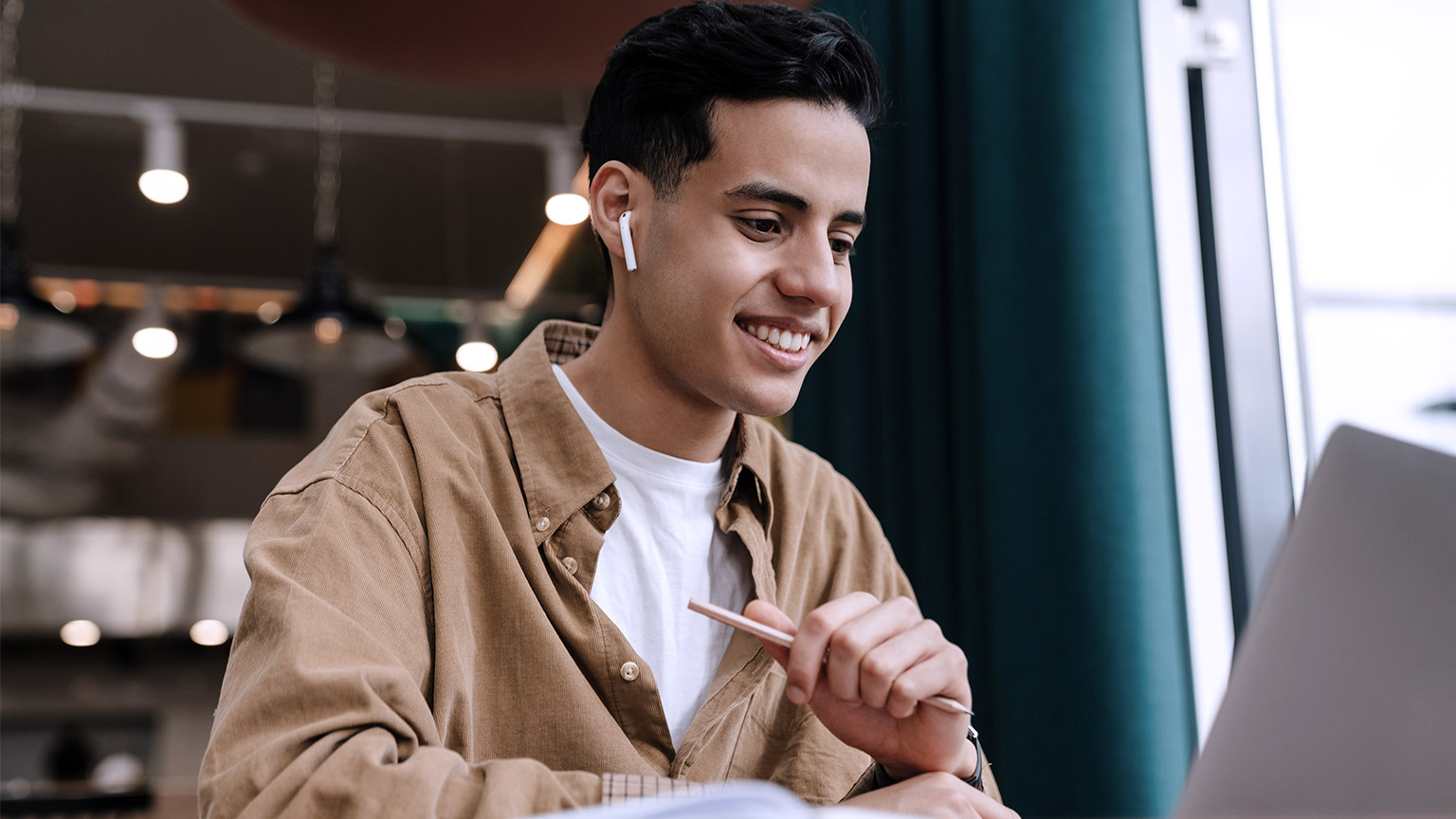 Young hispanic man watching at computer screen while smiling