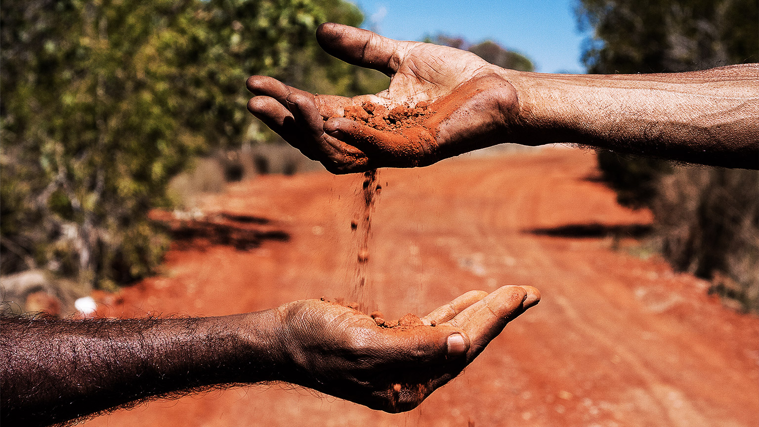 Australian outback background. Two hands passing red soil from one to another. Concept of Aboriginal people passing on values to next generation.