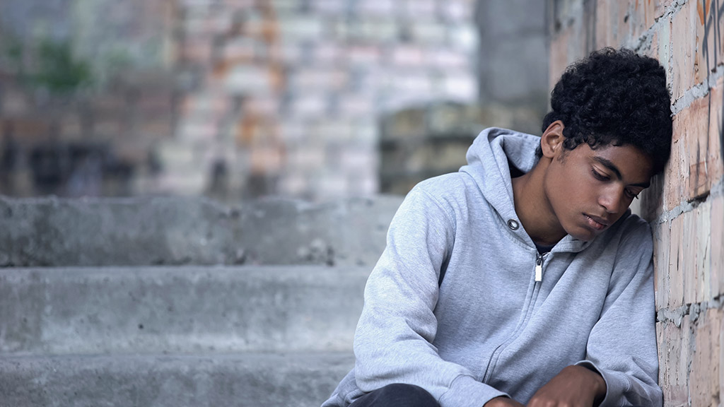 Depressed male teenager leaning brick wall sitting stairs