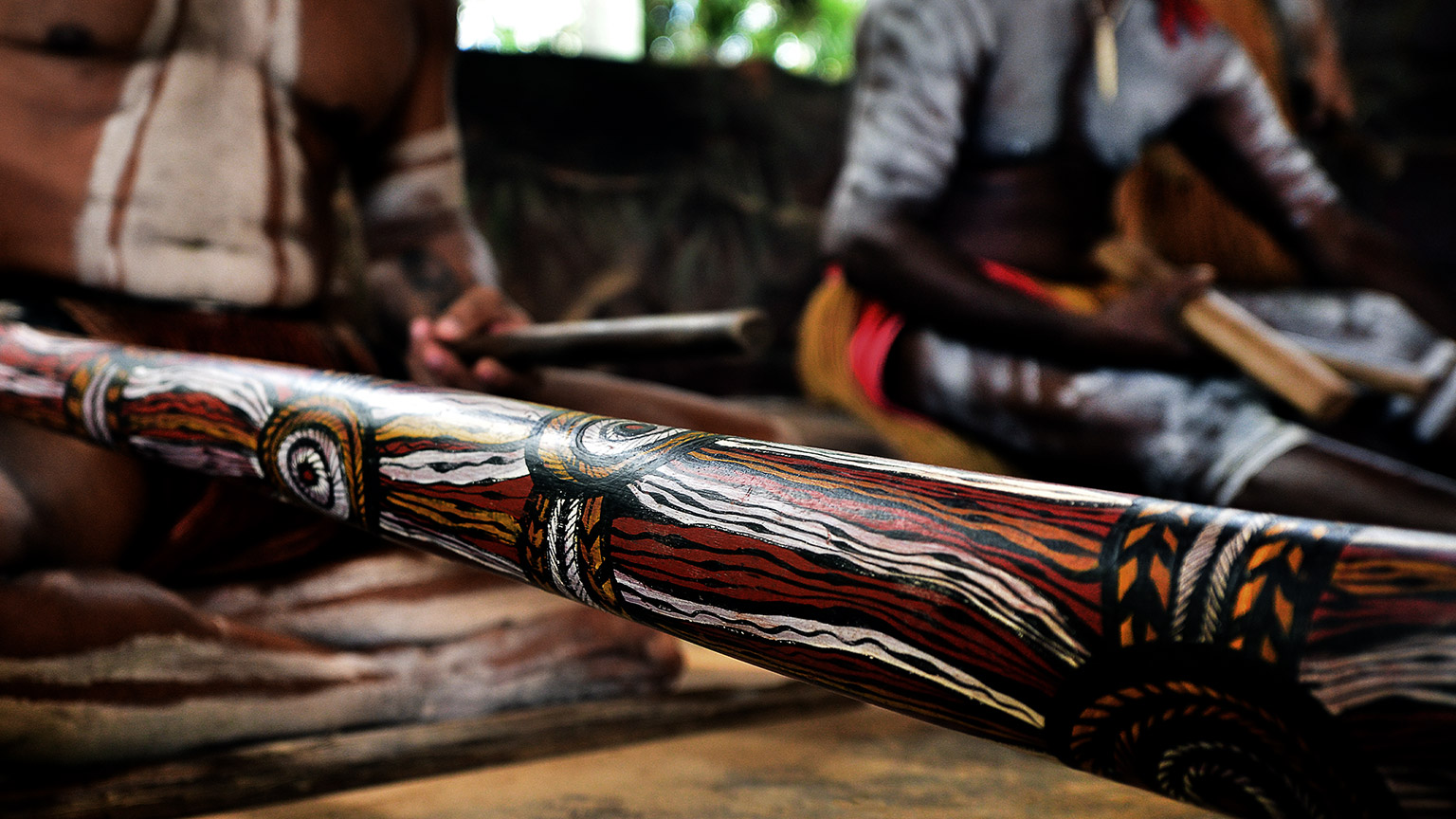 Australian Aboriginal men playing Aboriginal music on didgeridoo and wooden instrument during Aboriginal culture show in Queensland, Australia.