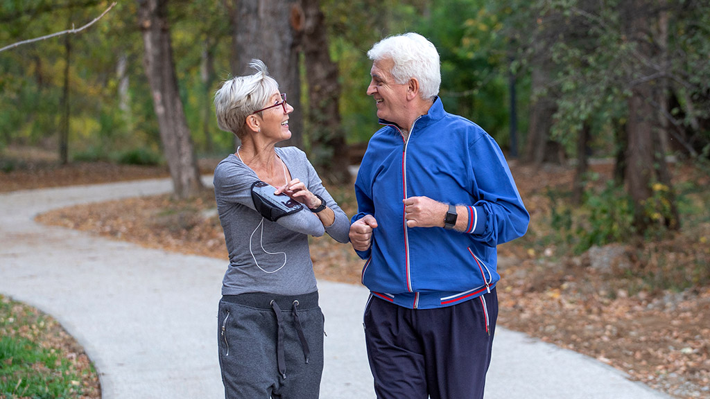 Active senior couple jogging in the park at autumng day and smile