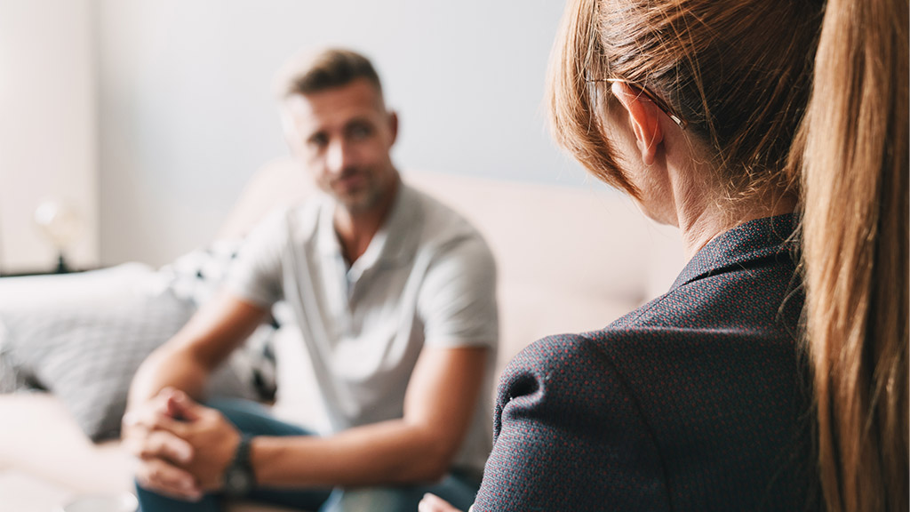 Photo of caucasian focused man having conversation with psychologist on therapy session in room