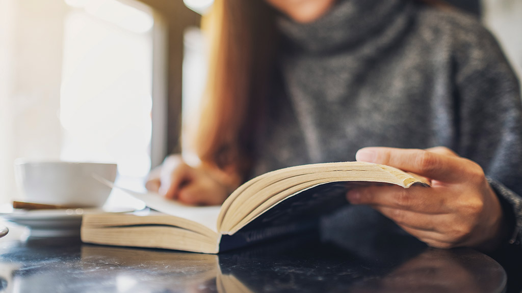 woman holding and reading a book with coffee cup on the table