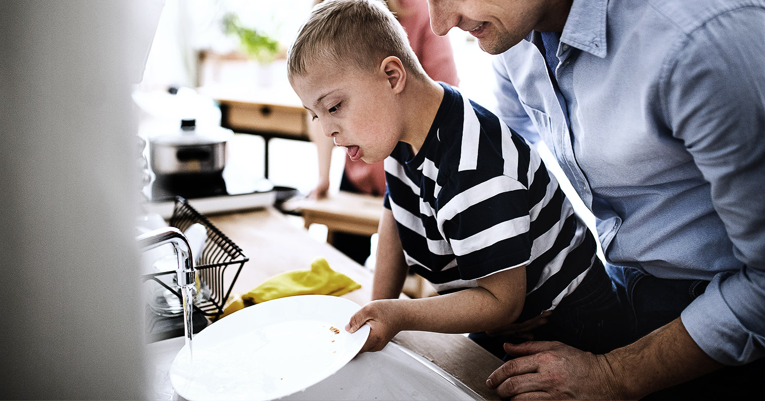 Persom with down syndrome patient indoors in kitchen, washing dishes.