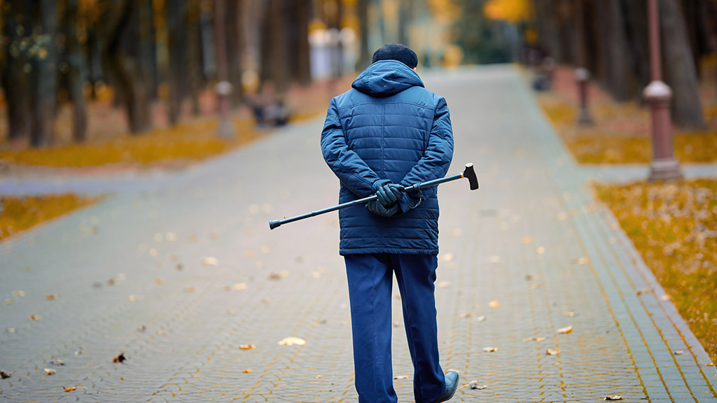 Elderly man walking with walking cane in hand behind his back