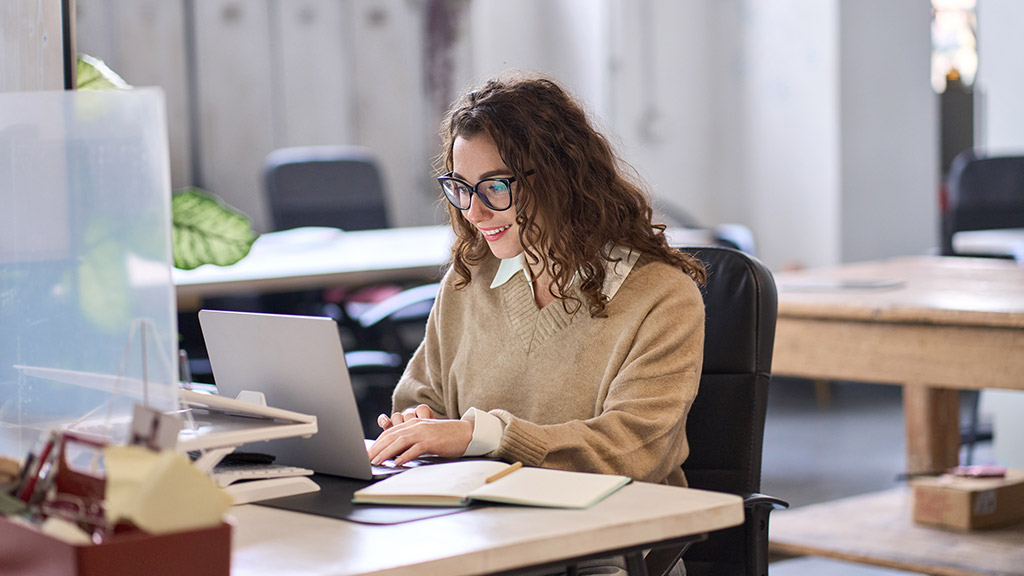 Young happy professional business woman employee sitting at desk working on laptop