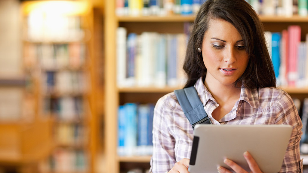 Young focused student using a tablet computer in a library