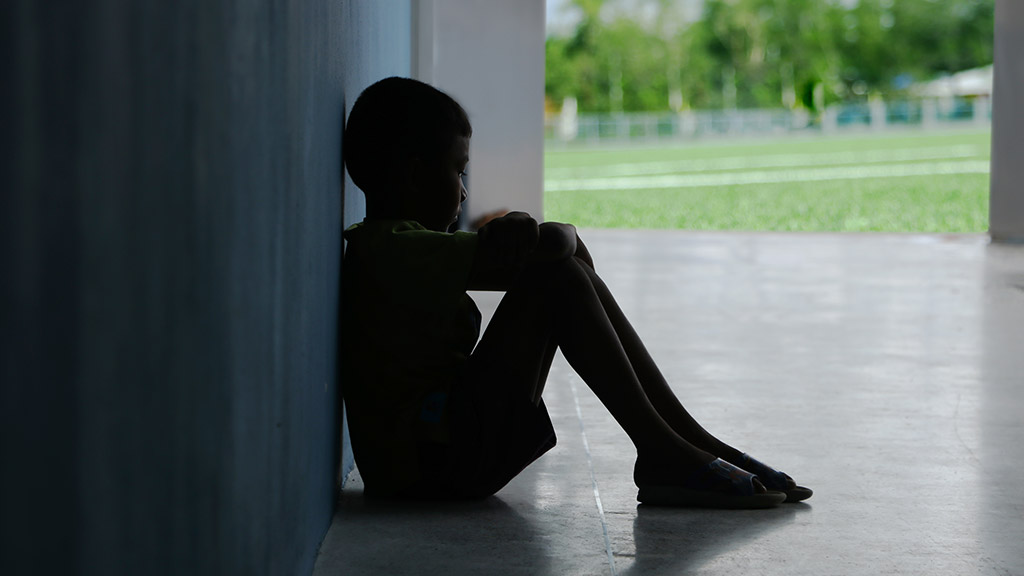 The boy who is upset and sits in the dark corner of the room