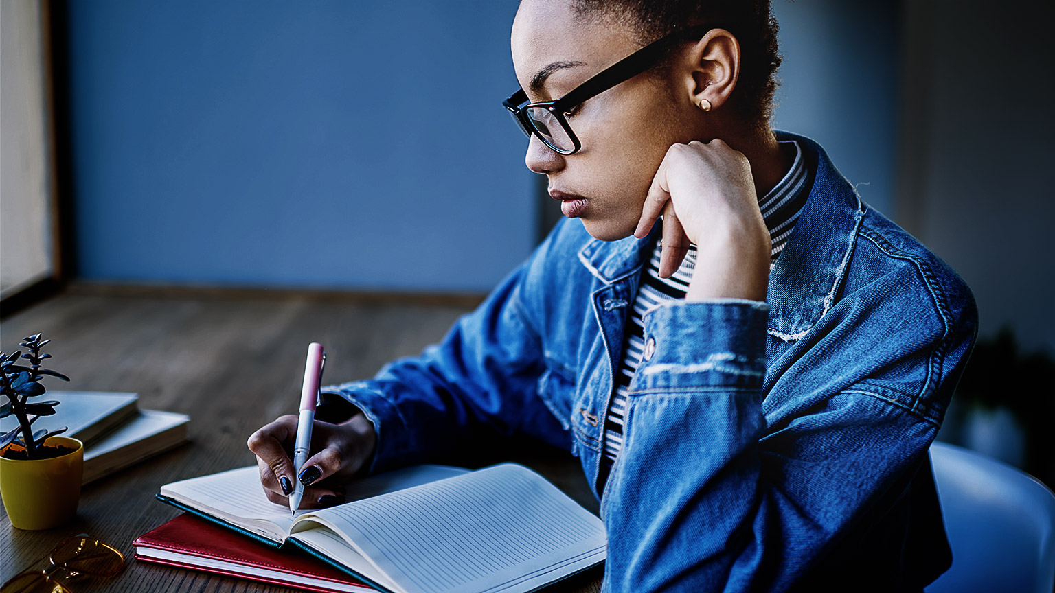 A person writing in a notebook while reflecting