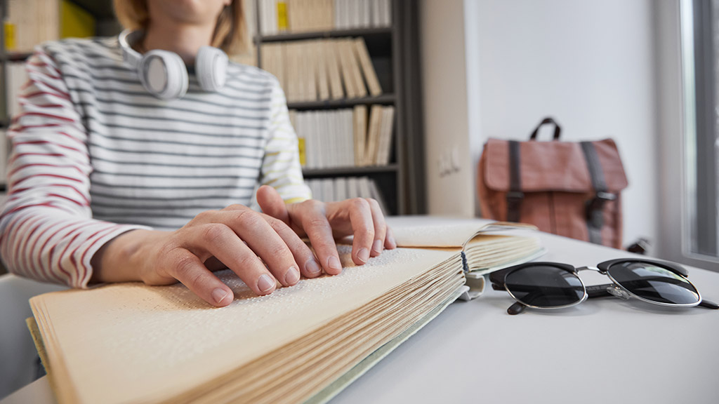 Close up of young blind woman reading Braille book in college library