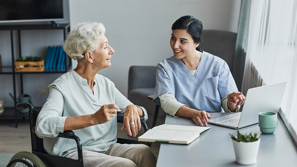 female nurse helping senior woman using laptop at home