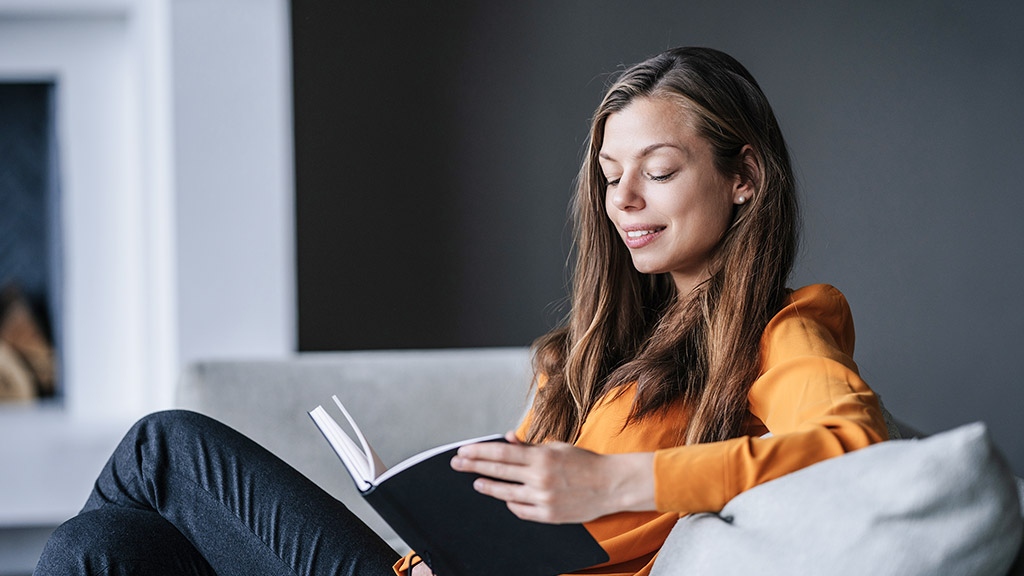 woman in orange blouse holding book, relaxing at home