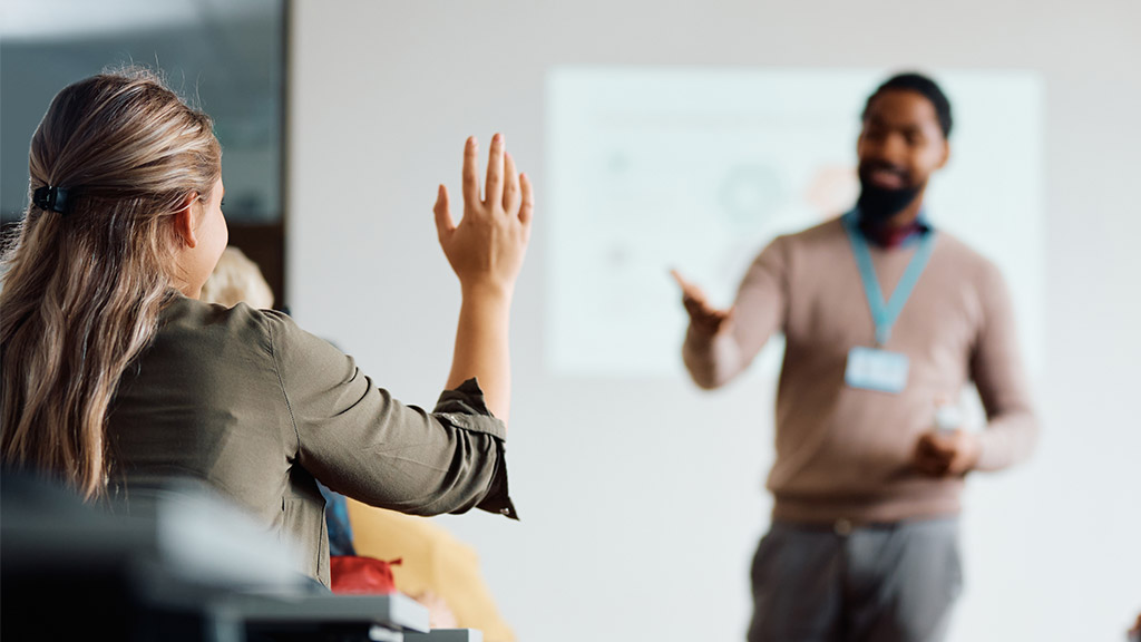 Back view of student raising her hand to answer teacher's question during education training class