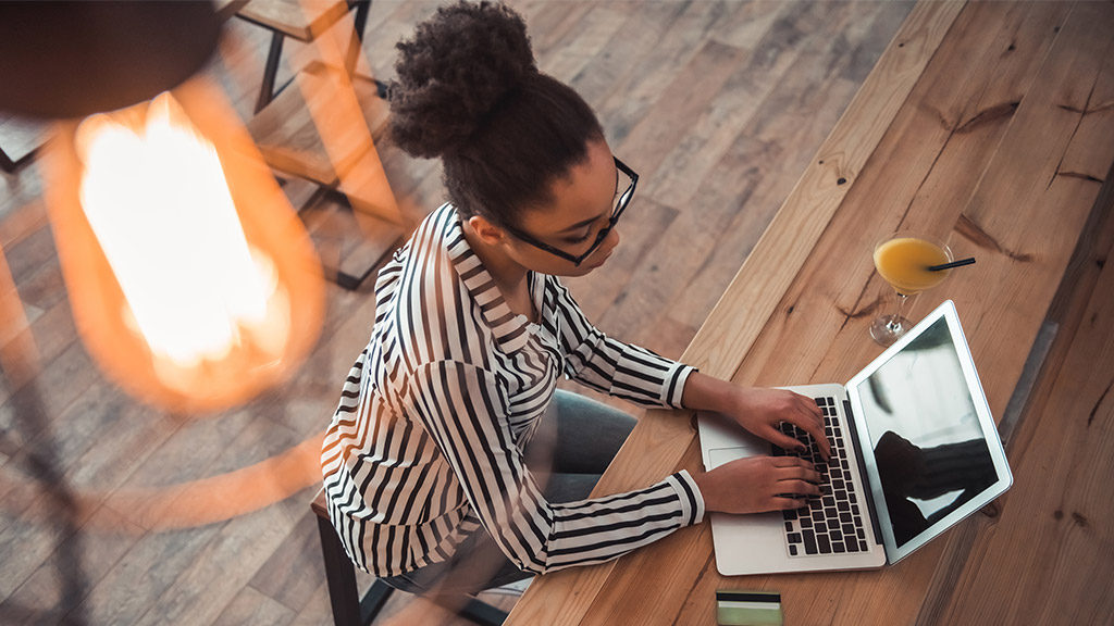 High angle view of beautiful Afro American girl in smart casual clothes and glasses working with a laptop in cafe