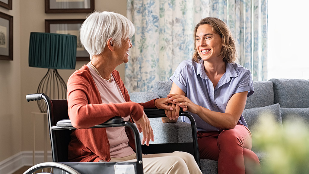 Mature woman comforting senior mom sitting on wheelchair at nursing home