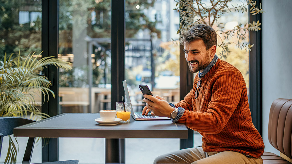 man using a phone in the cafe and working on the laptop