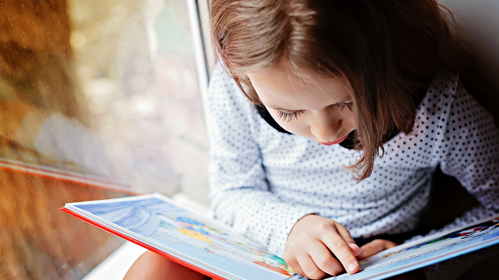 toddler girl with book near the window