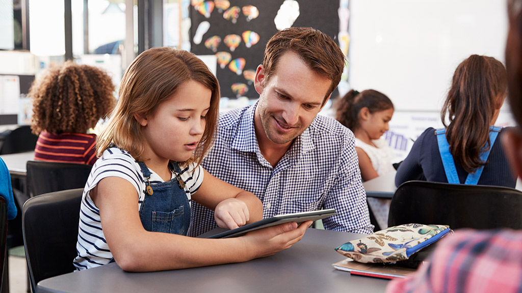 Teacher and young schoolgirl using tablet in classroom