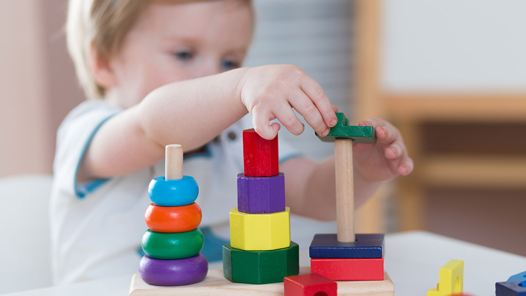 Two years old child boy playing with wooden colorful blocks and sorting shapes at home