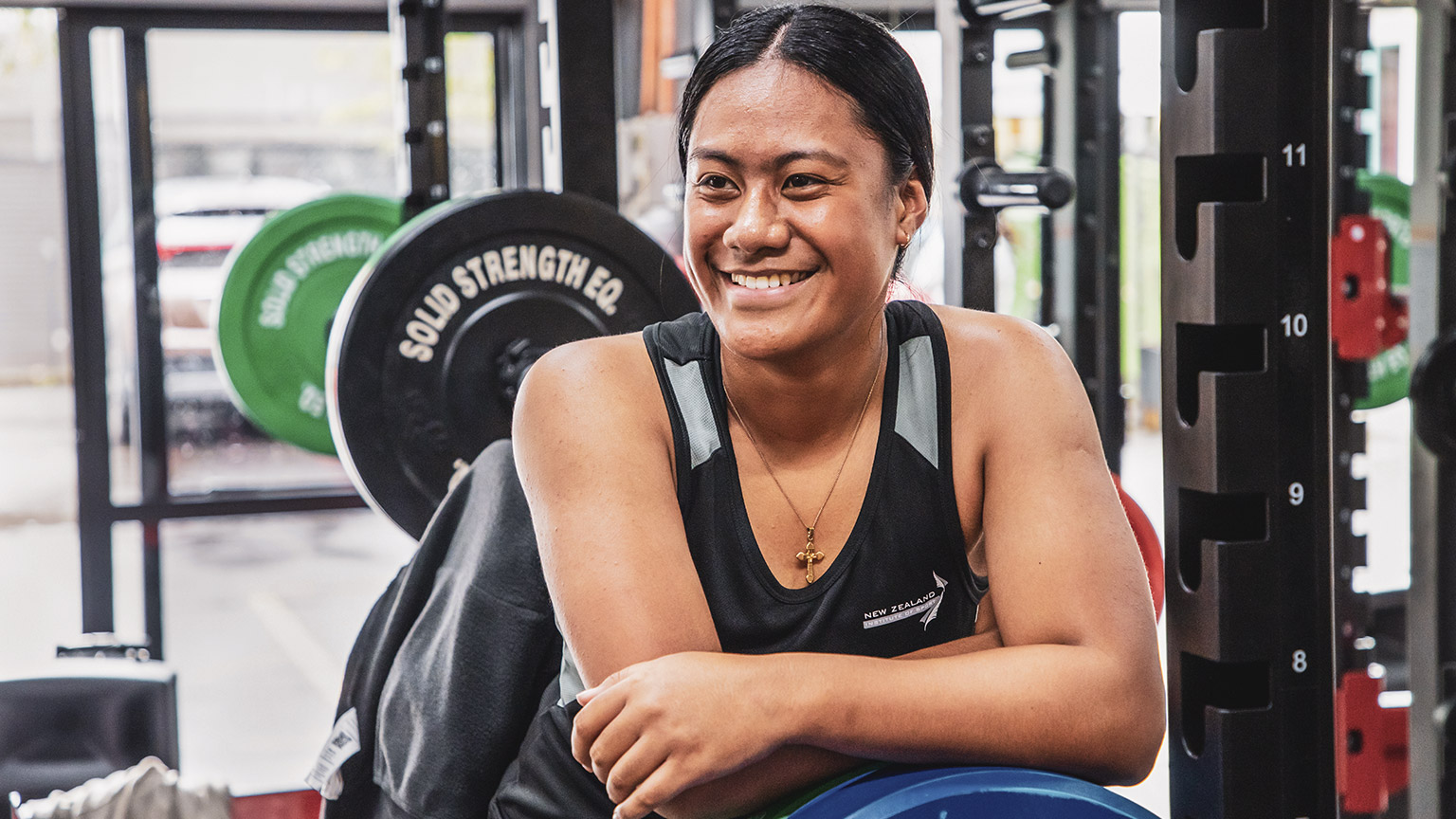 NZIS student smiling and leaning on a barbell weight in the campus gym