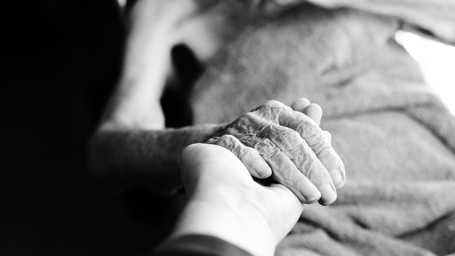 A person holding the hand of a dying patient