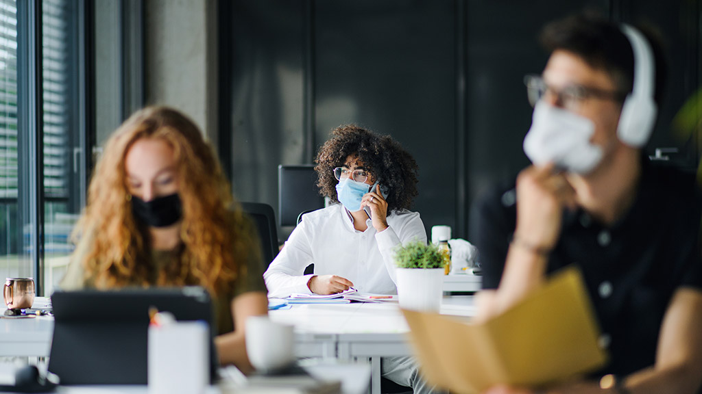 Young people with face masks back at work or school in office after lockdown.