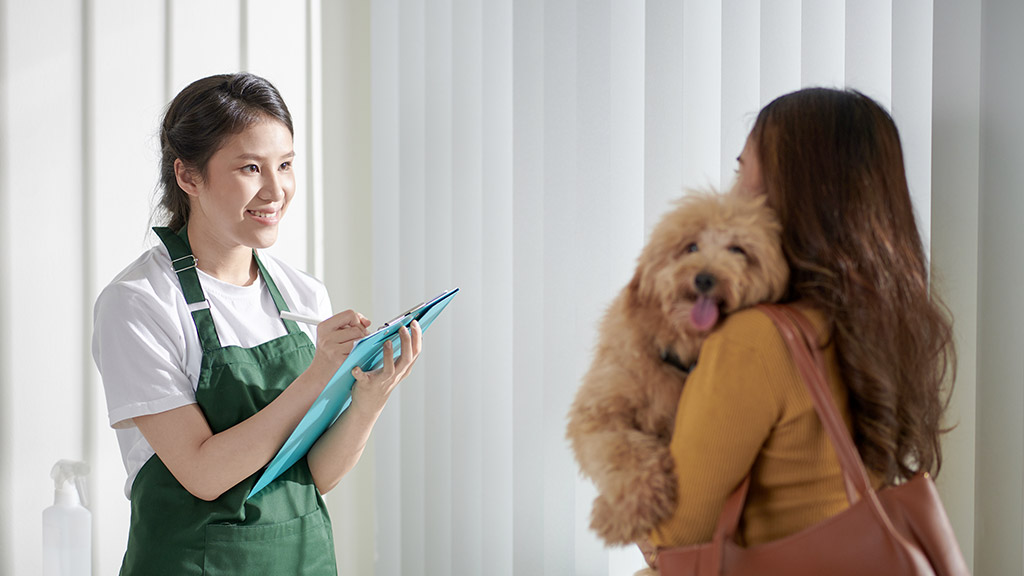 Cheerful female groomer filling form on clipboard when talking to dog owner