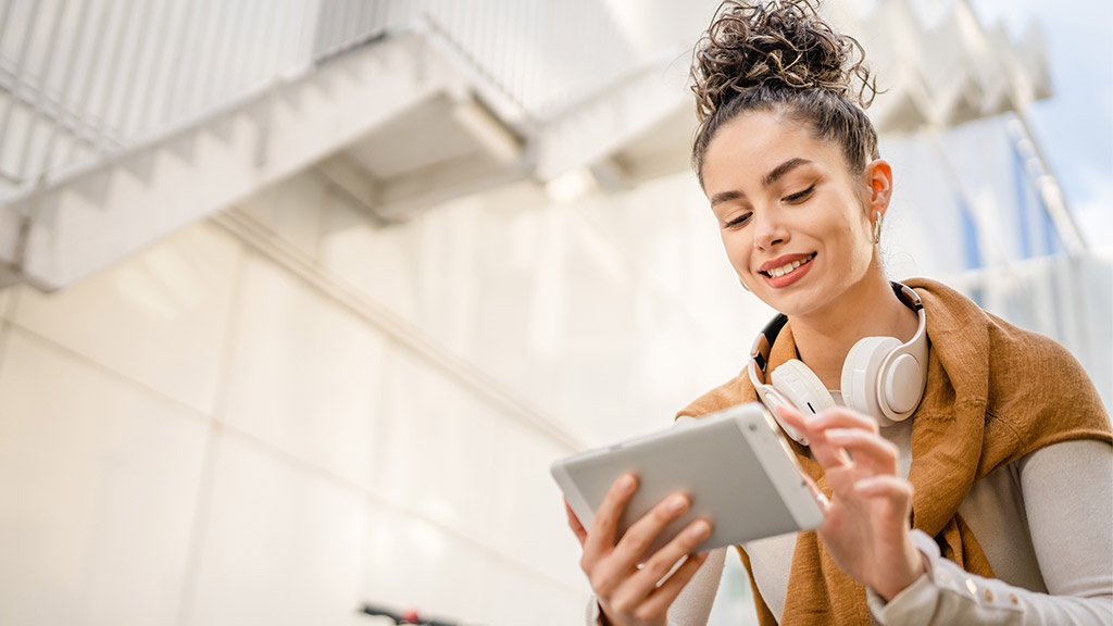 Young adult Caucasian woman student sit on bench outdoor in day in front of modern building use digital tablet