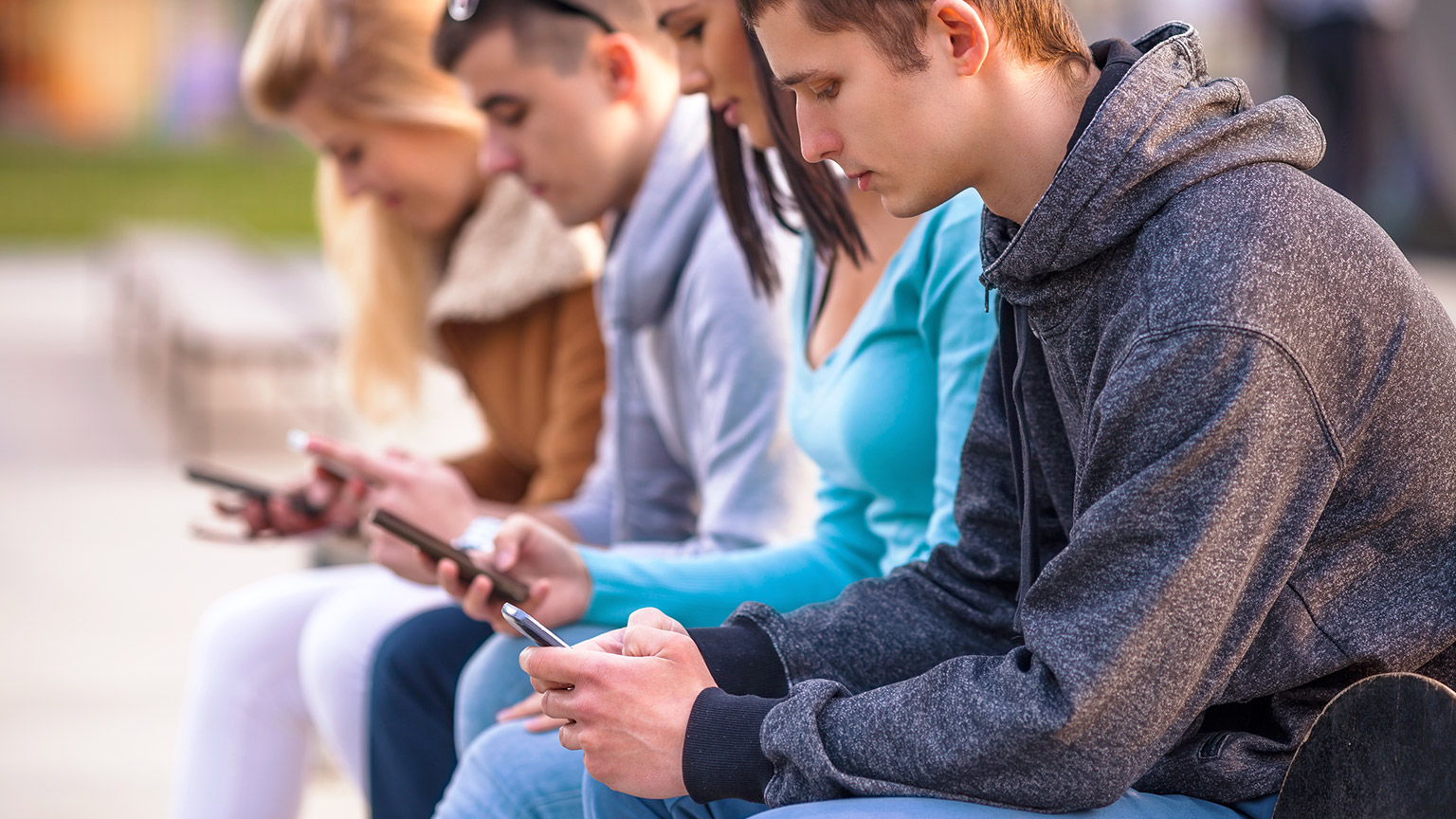 A group of teenagers sitting outside looking at their own phones