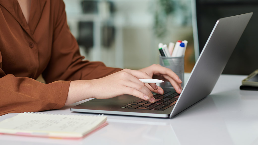 Hands of female entrepreneur working on laptop, checking e-mails and writing in planner