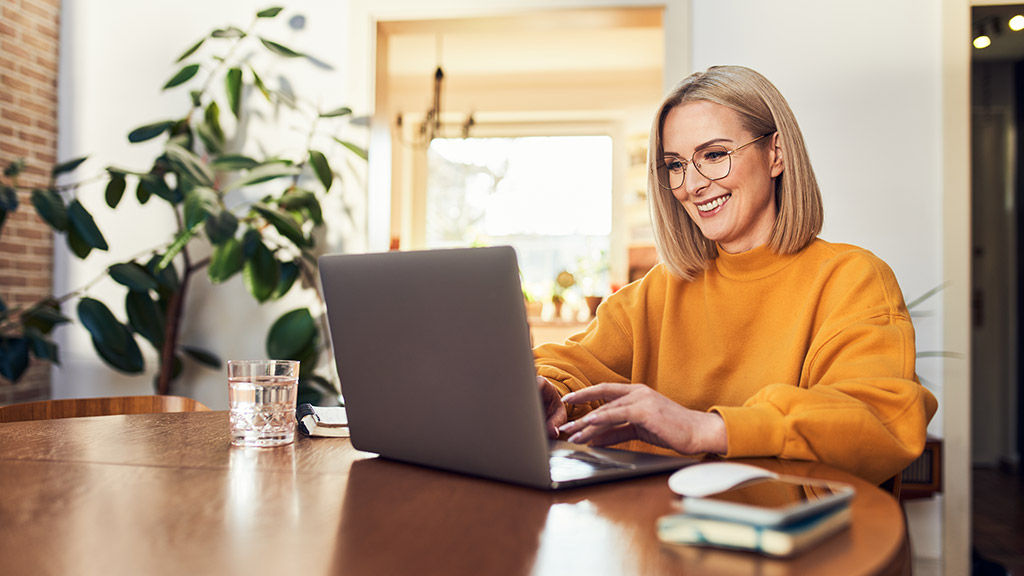 Happy mature woman using laptop while working remotely from home in living room