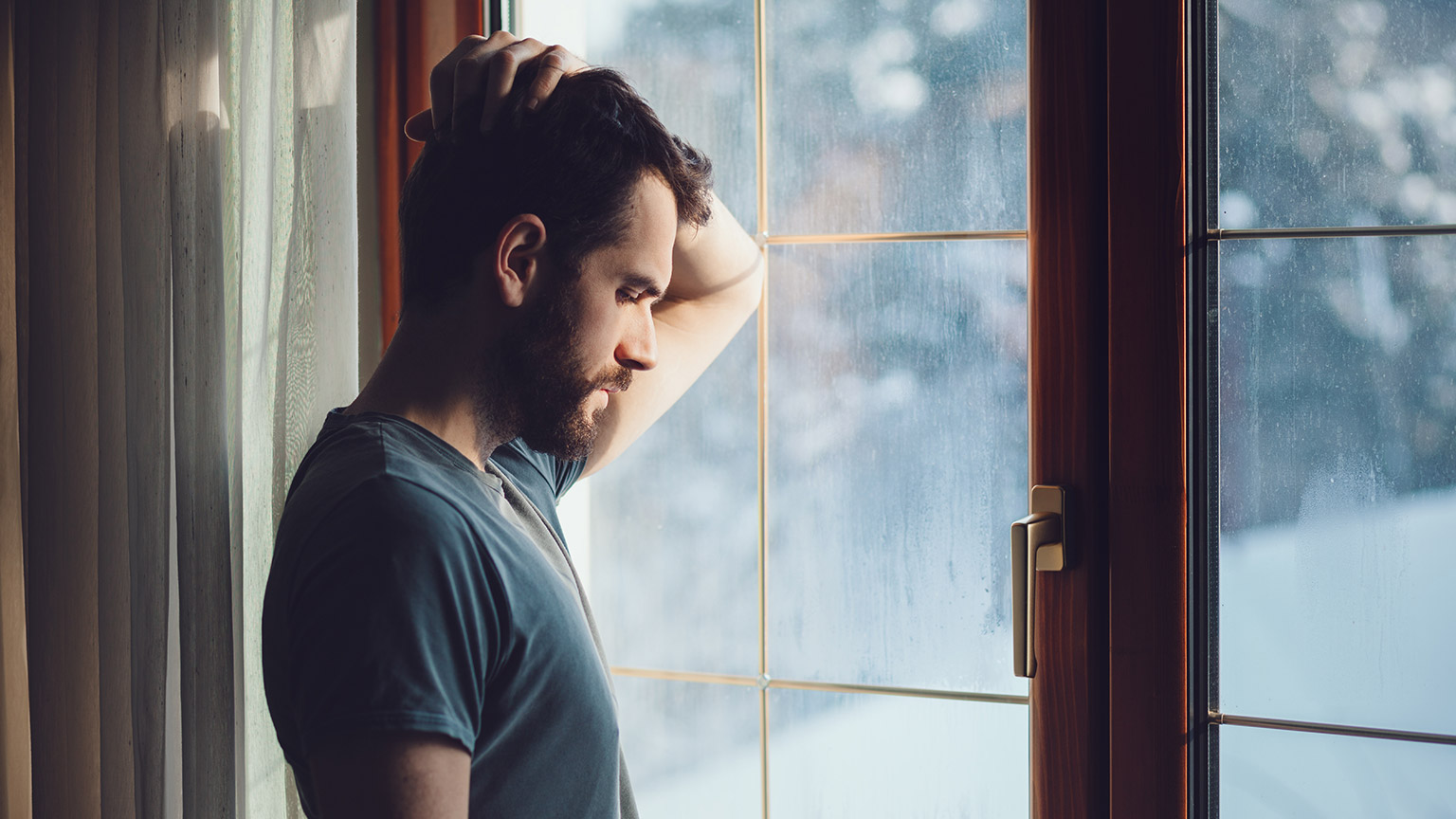 A person looking out a window with a sad look on their face