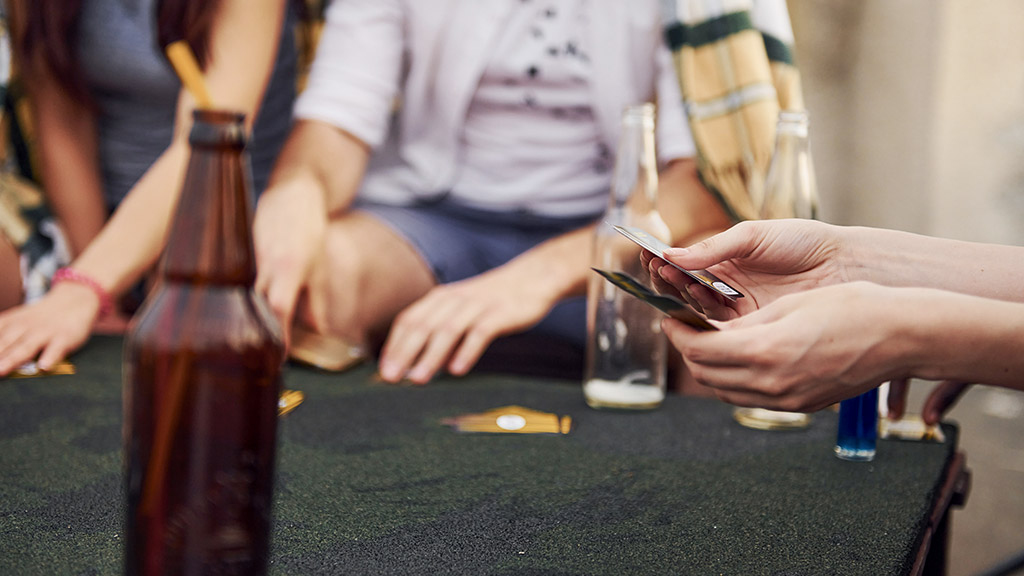 Sitting by table drinking alcohol while playing card game