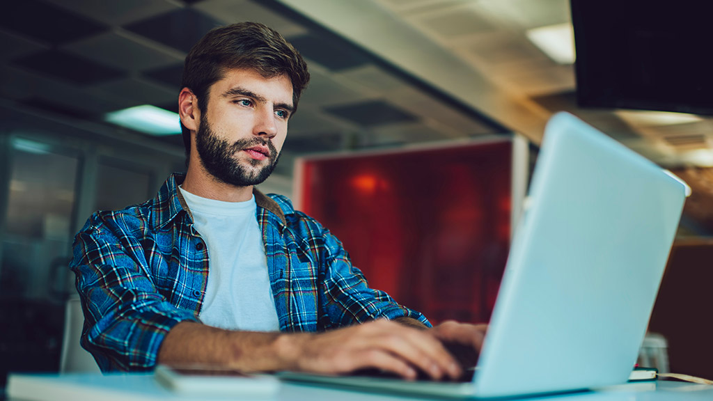 Caucasian male programmer creating software system via laptop application using coworking wifi internet