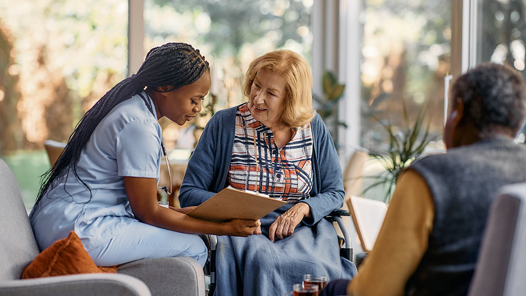 Nurse analyzing senior woman's medical record while talking to her at nursing home