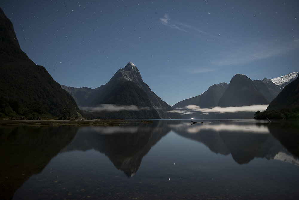 A photo by David Wilson from Milford Sound showing mountains, a lake, and stars