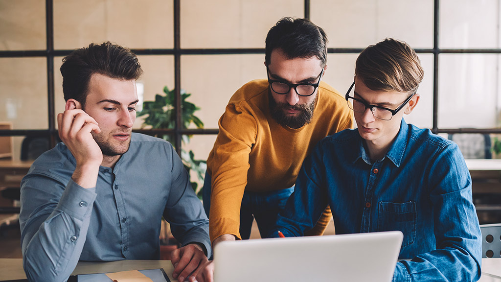 Group of young male coworkers watching webinar online via online application on modern laptop computer