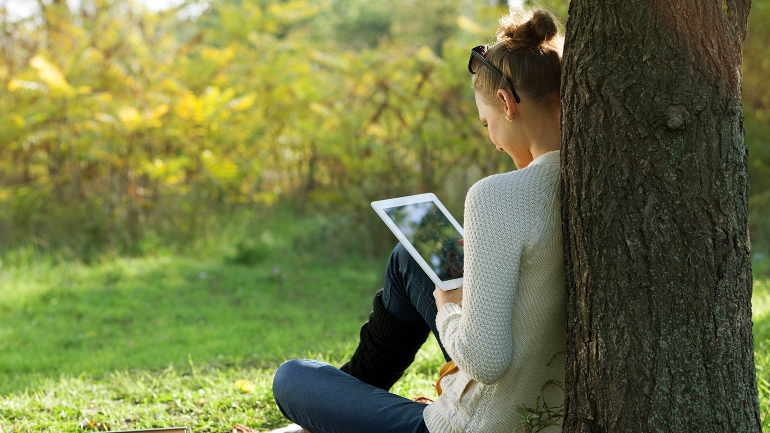 A person sititng outdoors reading on a tablet device