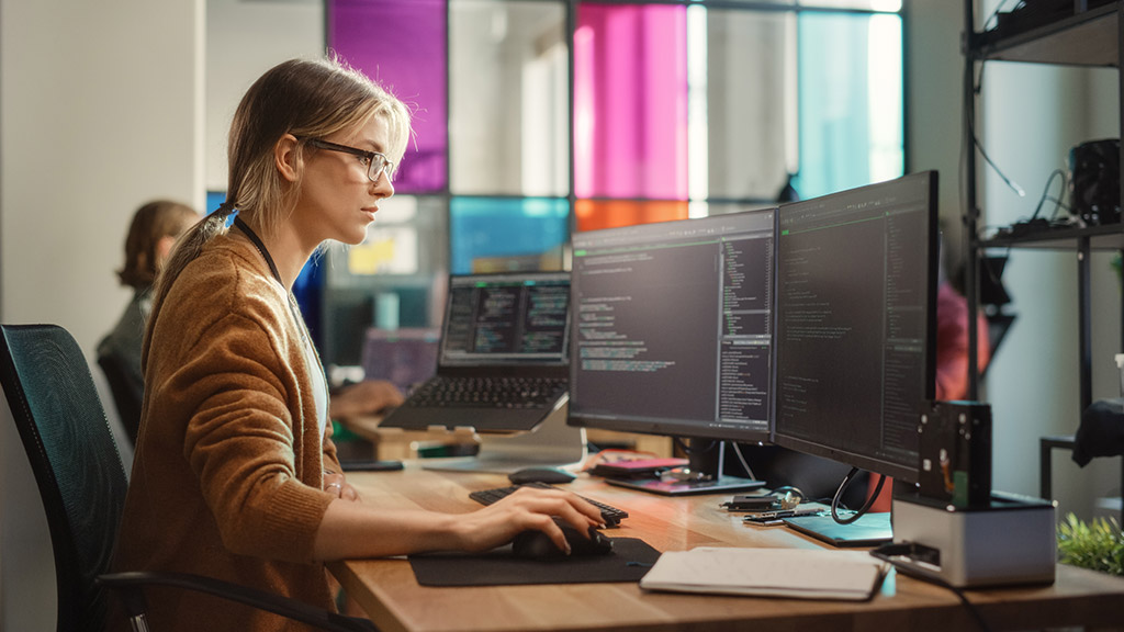 Caucasian Woman Coding on Desktop PC and Laptop Setup With Multiple Displays in Spacious Office