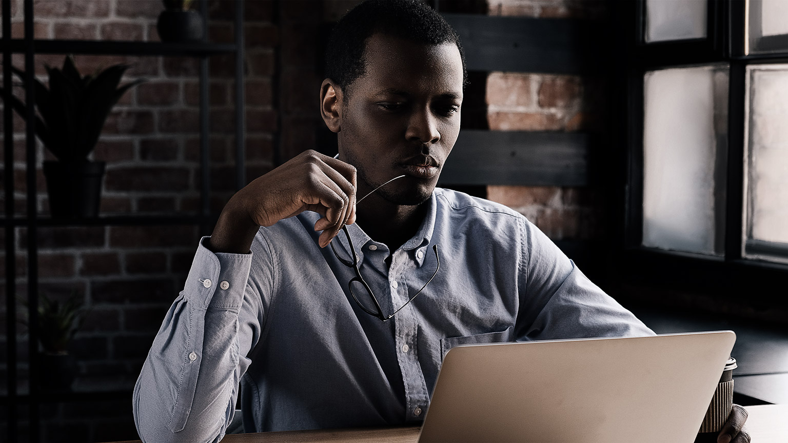  holding glasses while looking attentively at screen of laptop