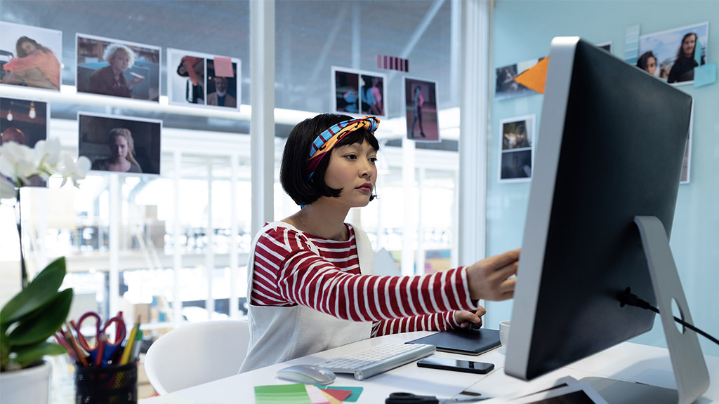 Front view of young pretty Asian female graphic designer using graphic tablet at desk in office. 