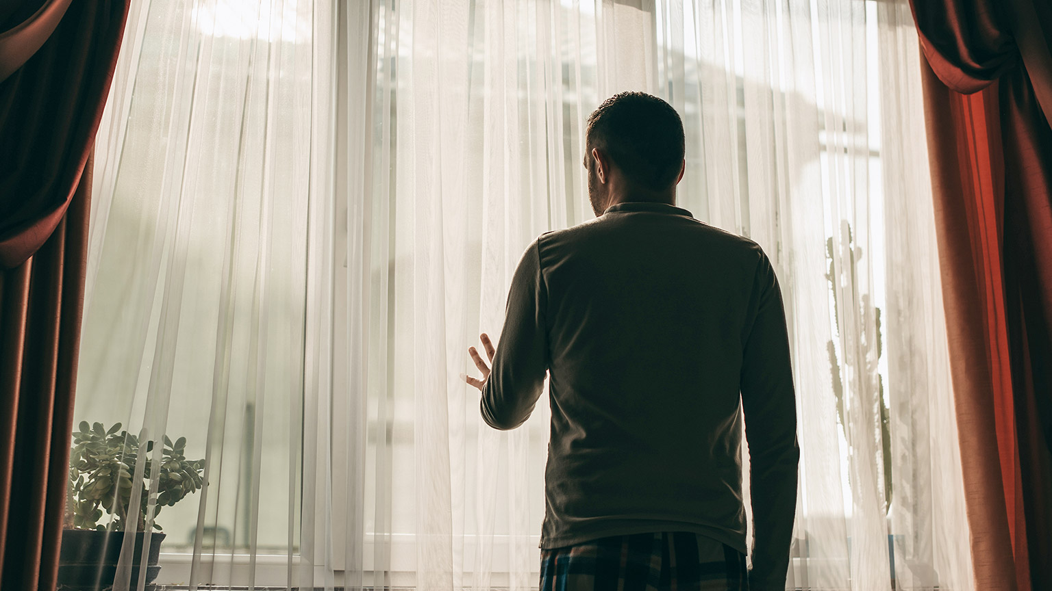 A young man stands by the window at home