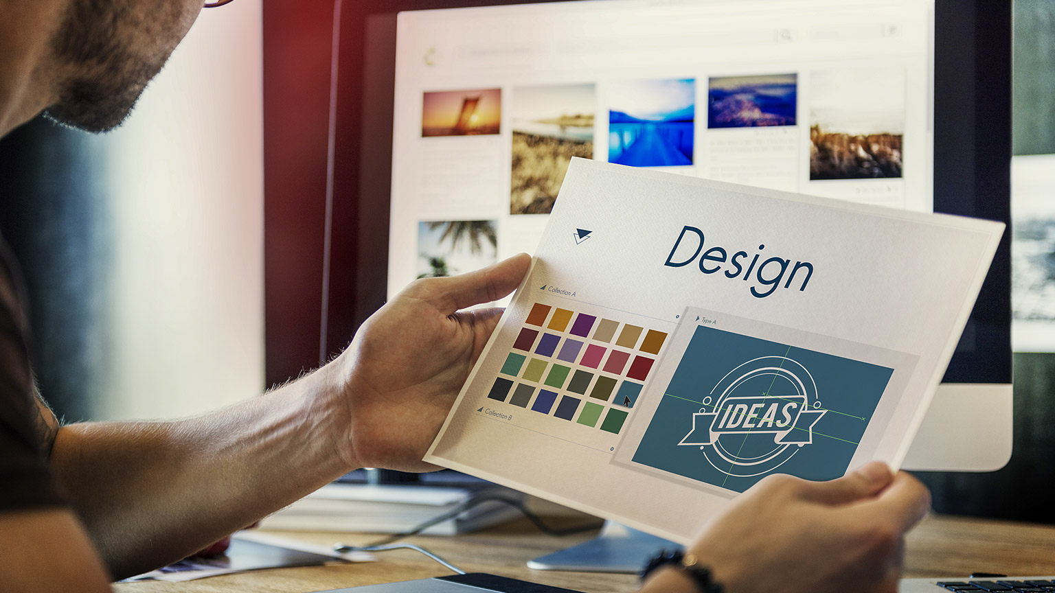 a man holding a printed design working at his workstation